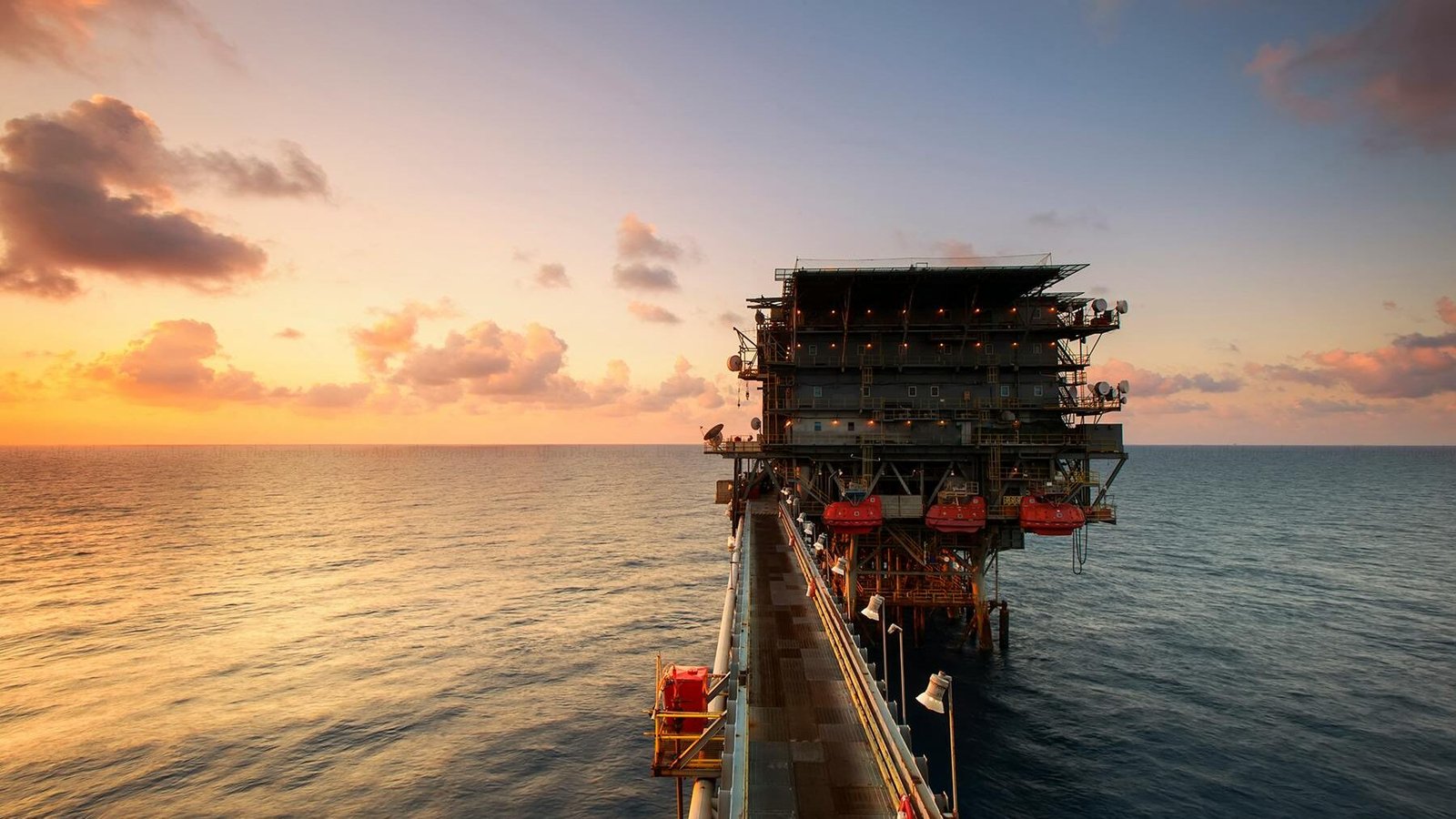 Nuestra Firma A breathtaking view of an oil platform on the ocean at sunset, showcasing industrial beauty.