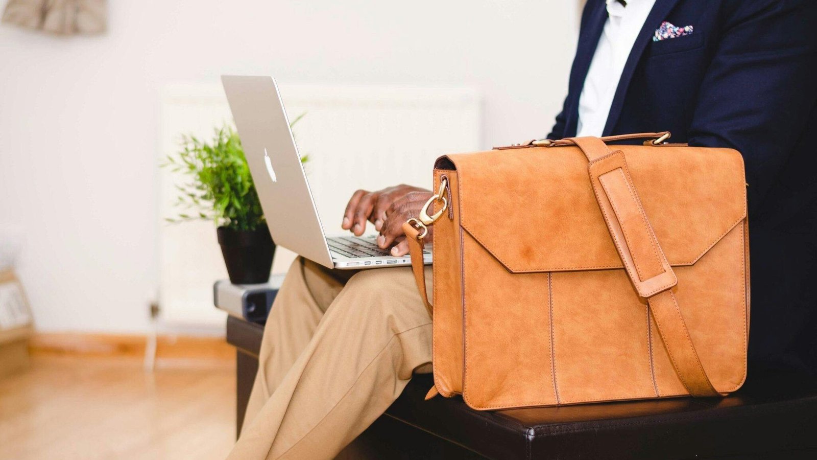 Nuestra Firma A stylish businessman working on a laptop indoor with a leather briefcase.